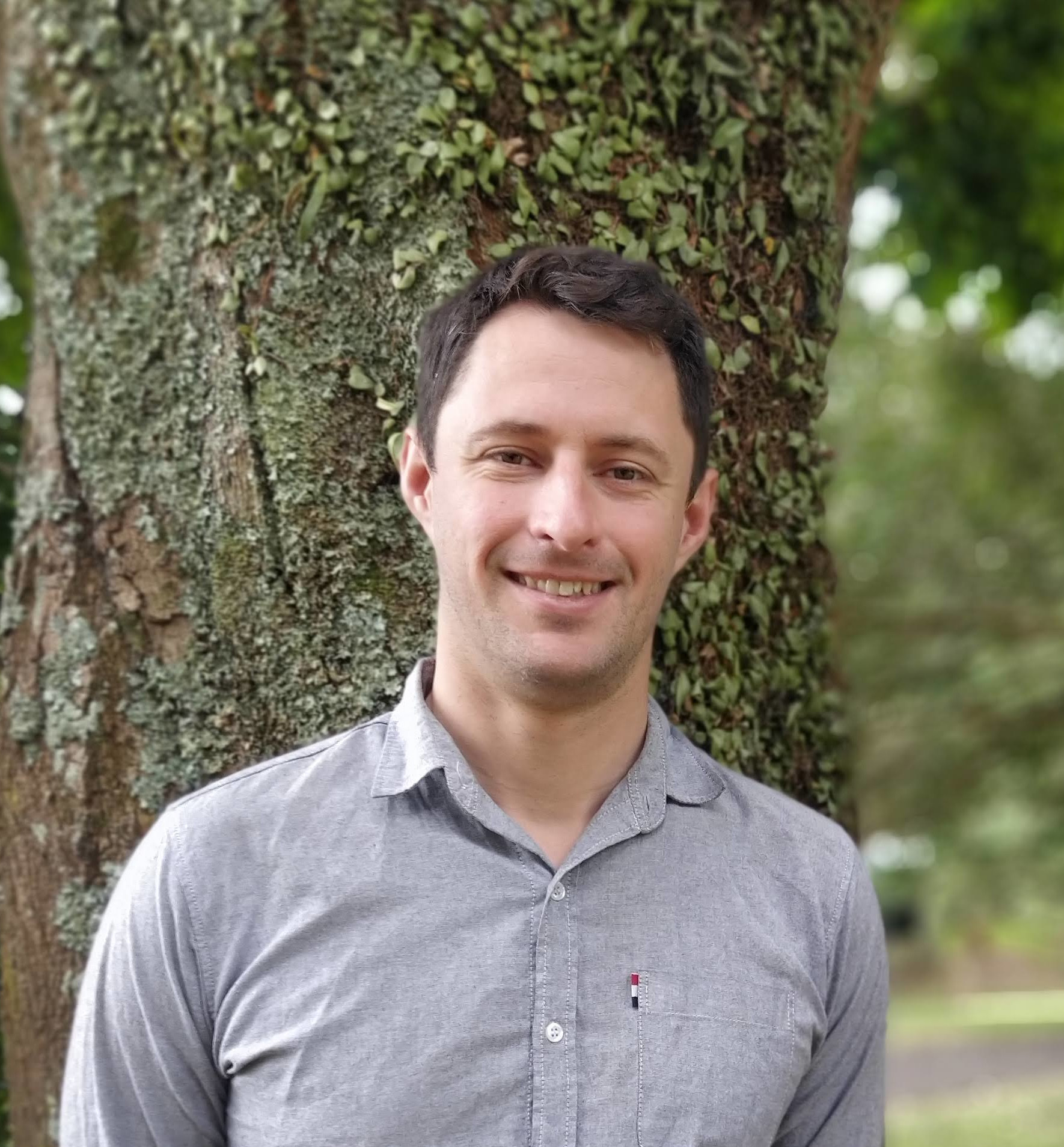 man with short dark brown hair in front of a tree